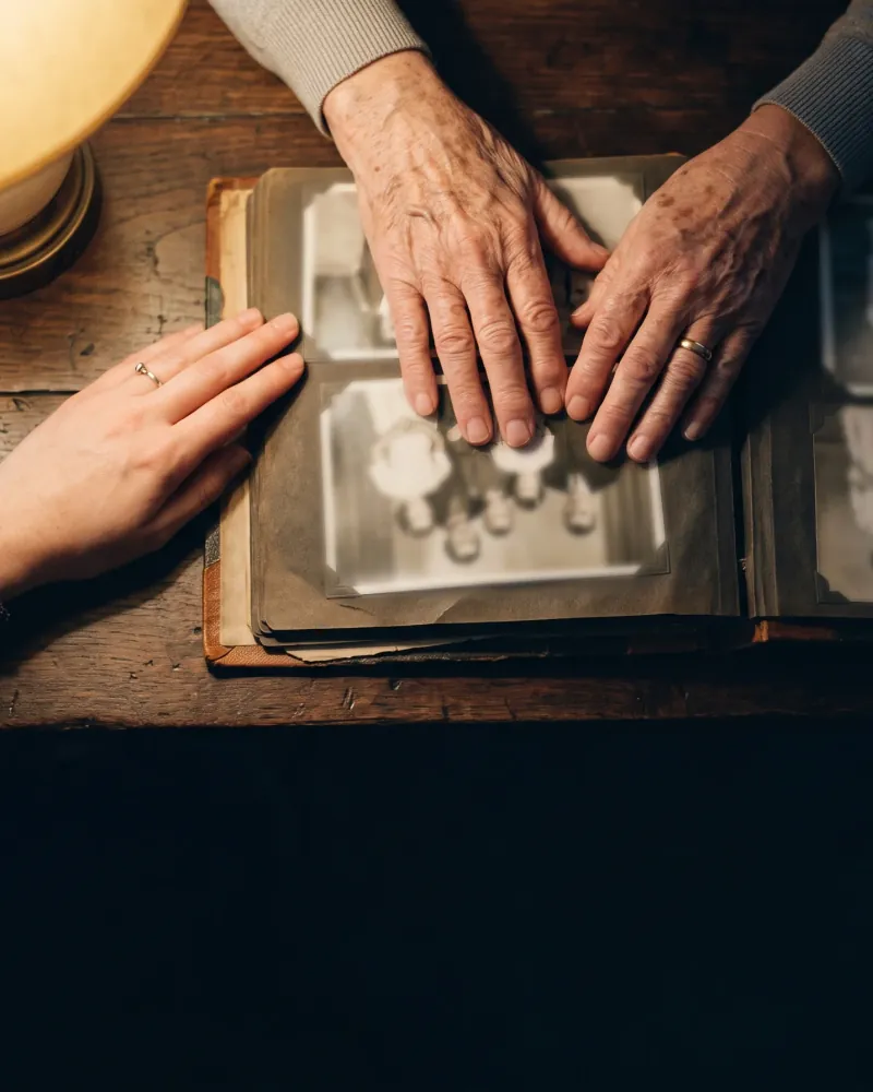 Las manos de una abuela y de su nieta sobre un álbum de fotografías familiares antiguas.